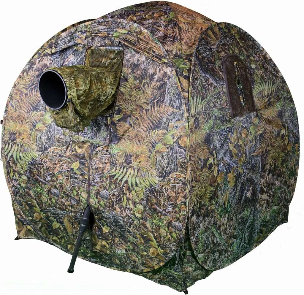 A camouflaged colored small tent with a lens sized hole in it.
