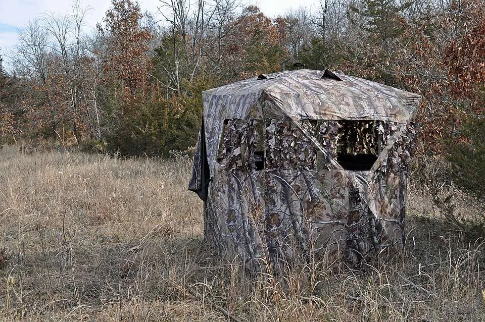 A camouflaged colored square tent with a lens sized hole in it.