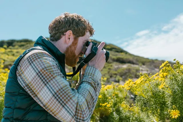 A man is photographing some yellow flowers.