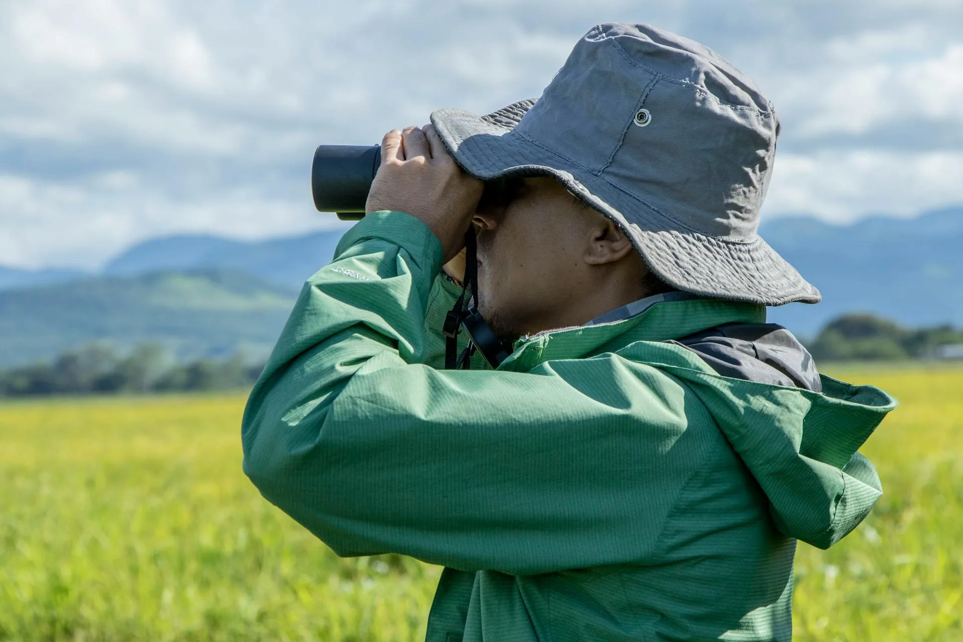 Man in a jacket and hat looking through binoculars.