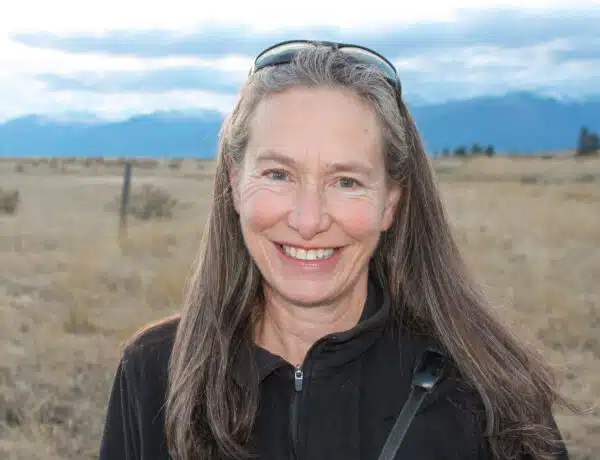 A woman with long hair stand in a pasture.